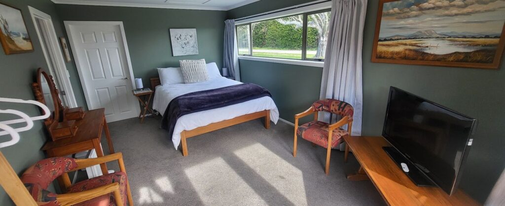 Cottage bedroom with queen bed, armchair and garden view